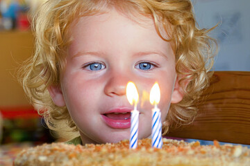 Happy male caucasian child blowing out birthday candles on cake