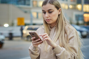 young blonde woman uses a mobile phone application to call a taxi in the evening city