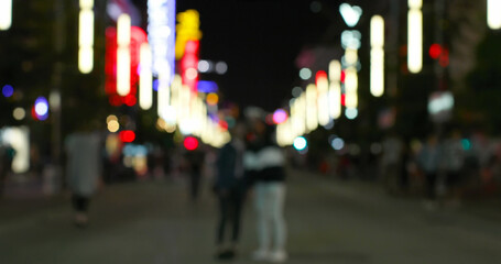 Image of defocussed shop and street lights, with people walking on a city road at night