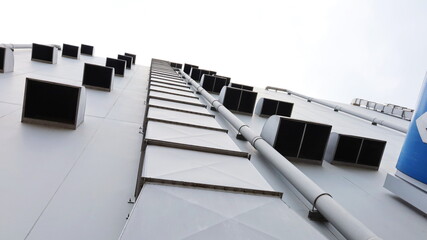 Ventilation pipe next to the building wall. Metal pipes with many vents of a department store for control and decontamination for safety on gray building background in bottom view. Selective focus