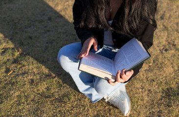 close up shot of young woman sitting in a park reading a book. Concept of hobbies, lifestyle and learning.