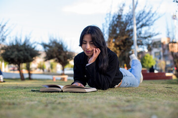 Young woman lying in a park reading a book. Concept of people and lifestyles.