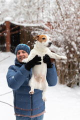 A man holds a jack russell terrier breed dog and throws it into the snow in winter. Vertical photo.