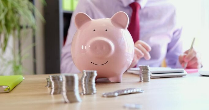 Pink piggy bank businessman saves money and counts bills on calculator