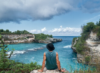 man sitting on the edge of a cliff with a view of a blue lagoon
