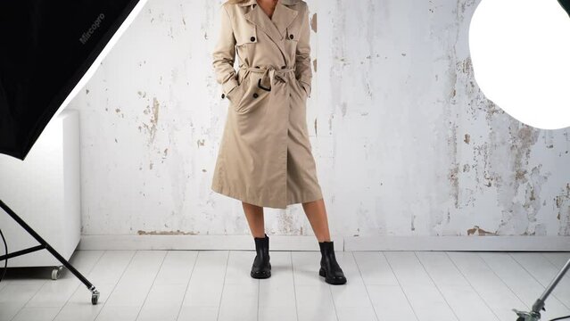 Female wearing beige coat and black boots walks in studio. Fashion and style concept. White wall backdrop.