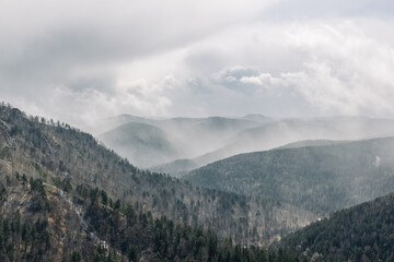 Breathtaking landscape with snowy clouds over mountains with sunbeams reflected in them. Stormy winter weather.