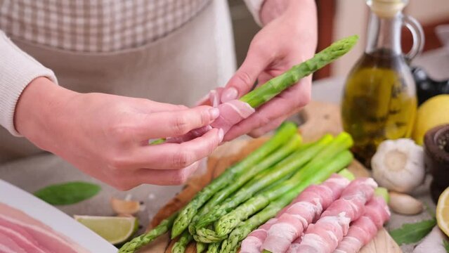 Woman Cooking asparagus wrapped with bacon at domestic kitchen