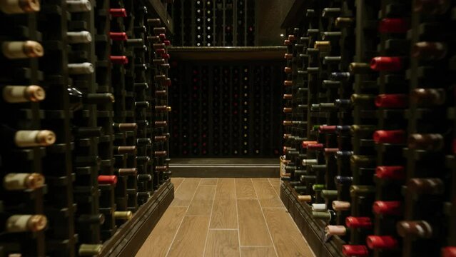 Slow motion pushing through rows of wine in dark home wine cellar