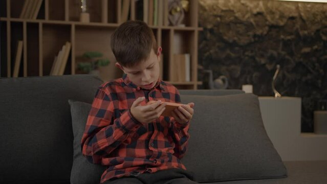 Autistic Kid Using Mobile Phone Sitting On Couch Alone At Home.