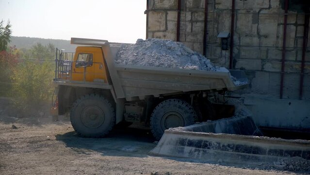 The mining dump truck backs up and pours the stone into the bunker. Side view
