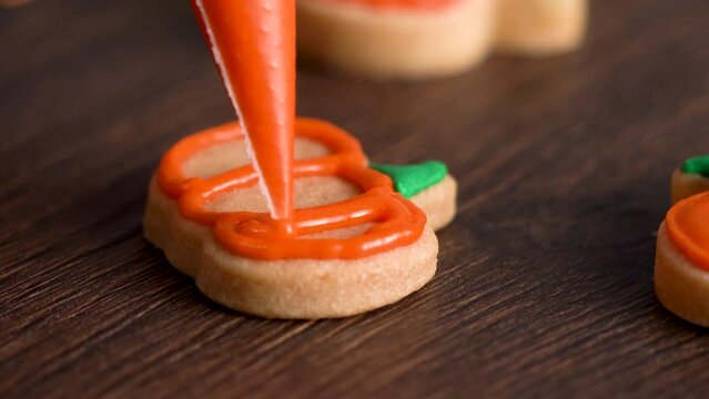 Decorating cute Halloween pumpkin cookies with frosting in icing bag.