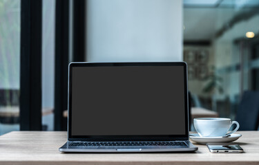 Mockup of laptop computer with empty screen with coffee cup and smartphone on table of the coffee shop background,ฺ Black gray screen