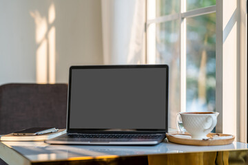 Mockup of laptop computer with empty screen with coffee cup and smartphone on table beside the window of the coffee shop background,Black gray screen