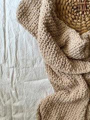 Top view of a woven rattan tray and a knitted plush beige plaid on a white bed. Minimalism