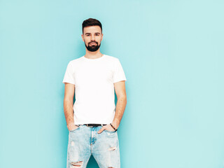 Portrait of handsome smiling model. Sexy stylish man dressed in white shirt and jeans. Fashion hipster male posing near blue wall in studio. Isolated