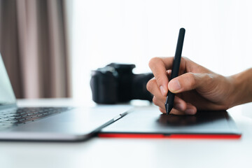 Graphic designer or Photographer use pen mouse drawing and retouch on a tablet board.