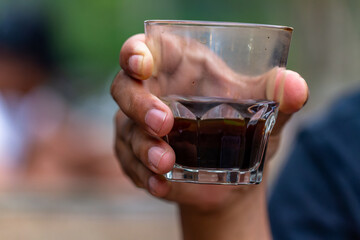 A hand holding a clear glass cup containing americano coffee