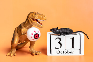 Toy dinosaur Tyrannosaurus holding eye in its paws, Calendar date 31 October isolated on orange background Holiday greeting card Happy Halloween day creative minimal concept