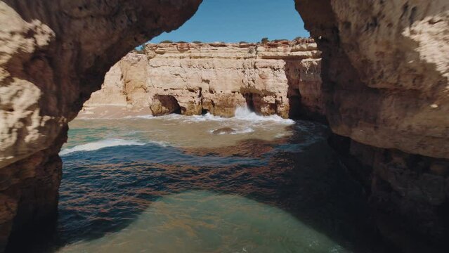 Drone pull back through a natural archway made out of rock. Ocean flowing in the surrounds. Taken at the Alba Resort in Algarve, Portugal.