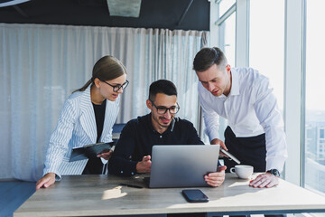 A team of businessmen in formal wear discussing project details and looking at laptop screen while collaborating during a meeting in a modern boardroom. Modern office
