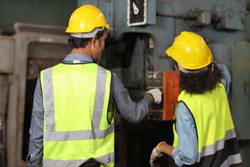 Rear view technician engineer or worker man and woman in protective suit standing and repairing operation or check industry machine process with safety hardhat at heavy industry manufacturing factory