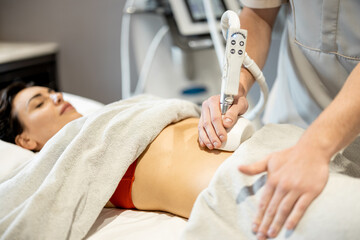 Fototapeta premium Woman receiving vacuum roller massage for her belly at medical beauty centre. Anti-cellulite and lymphatic drainage massage procedure
