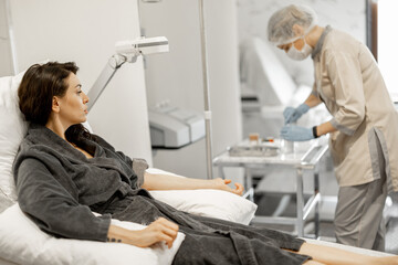 Woman in bathrobe sitting relaxed during blood washing procedure. Nurse preparing dropper and...