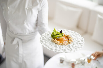 Chef holds a plate with delicious vegetarian meal decorated with flower made of avocado at...