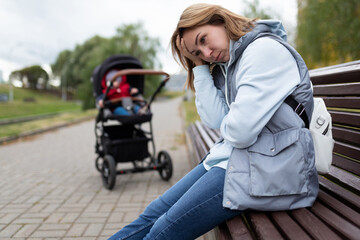 Fototapeta na wymiar young woman mother of postpartum depression sits with built-in feelings in the park on a bench next to a baby stroller
