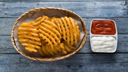 Fresh waffle fried french fries with chilli sauce and mayonnaise on wooden grey background