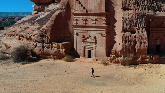 Aerial view of a person walking in front of Nabataean city tombs of Madain Salih in Saudi Arabia - descending, tilt, drone shot