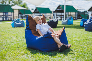 A cheerful child is playing on colorful beanbag chairs on the street. A little boy watches cartoons on a laptop while sitting on a chair in the park
