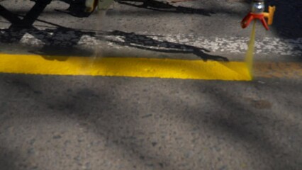 Closeup, slow-motion panning view of a line striper machine painting yellow stripes on a bicycle lane