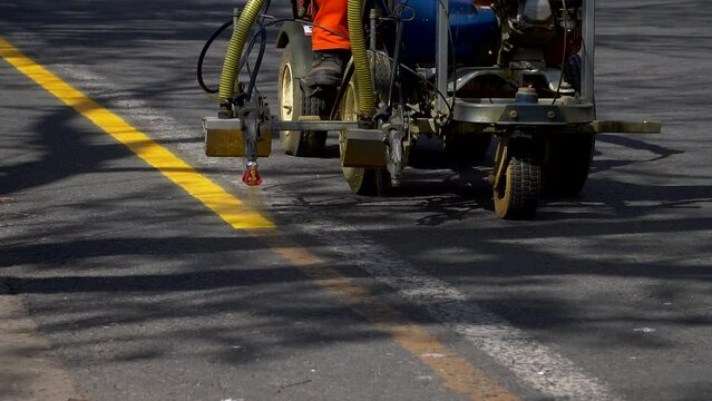 A line striper machine painting yellow stripes on a bicycle lane. Slow-motion, handheld.