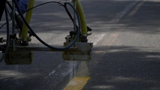 Closeup, slow-motion view of a line striper machine painting yellow stripes on a bicycle lane