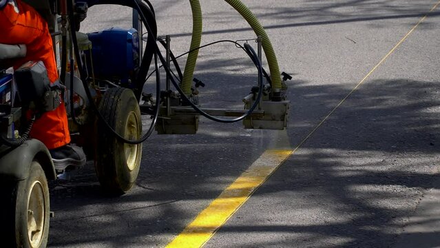 Slow-motion view of a line striper machine painting yellow stripes on a bicycle lane