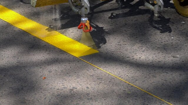 Closeup, slow-motion view of a line striper machine painting yellow stripes on a bicycle lane