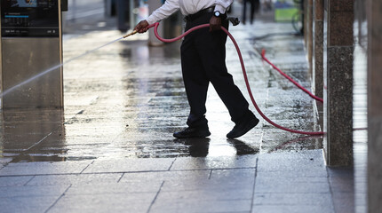 A worker washes the sidewalk in front of a restaurant in New York in the early morning