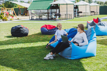 Fototapeta premium Mother and son on a soft bean bag chair. Mom and son in a bag chair in nature.