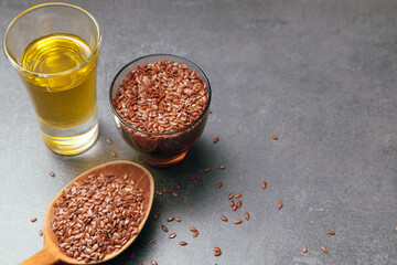Flax seeds in bowl and flaxseed oil in glass on gray stone textured background, close-up, selective focus. Linseed oil