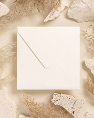 Square envelope near beige travertine stones and dried pampas grass top view, greeting mockup