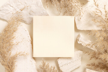 Blank card near beige travertine stones and dried pampas grass top view, greeting mockup