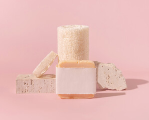 Soap bar with blank label and loofah sponges near stones on light beige close up. Mockup
