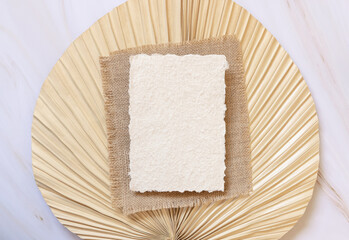 Blank handmade paper card on dry beige palm leaf near hare's tail grass top view,  boho wedding mockup