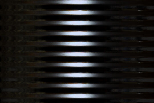 The outer side of a shiny round corrugated tin metal container with dark edges and a bright, vertical central highlight creating a dramatic, cold, alien type of image, captured in a studio 