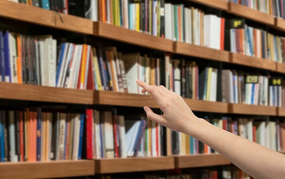 woman hand touching books in front of bookshelf, close up
