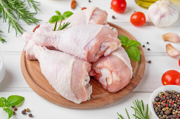 Raw uncooked chicken legs on a cutting board on a white wooden background. Meat with ingredients for cooking