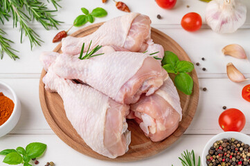 Raw uncooked chicken legs on a cutting board on a white wooden background. Meat with ingredients for cooking