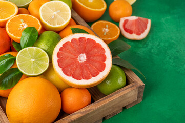Different citrus fruits with leaves in a wooden box on a concrete background. Healthy food. Top view